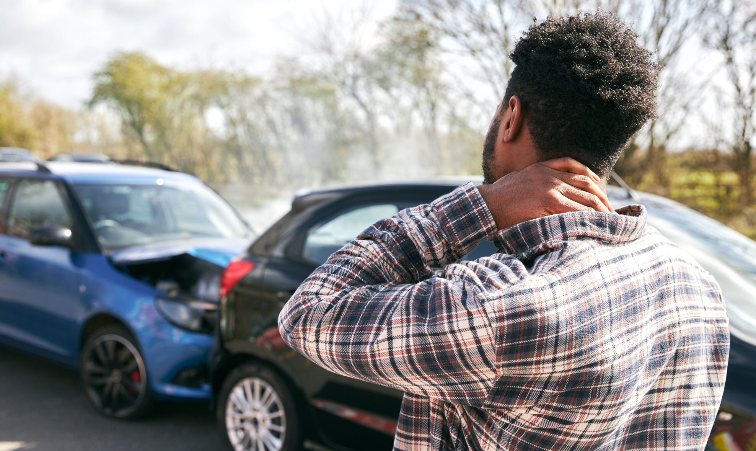 man rubbing neck near car accident